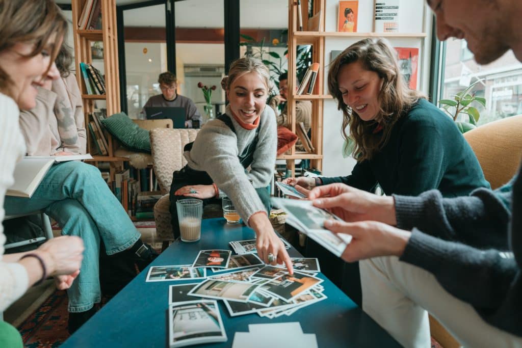 Mensen zitten om een tafel met kaartjes. 1 iemand wijst naar de kaartjes