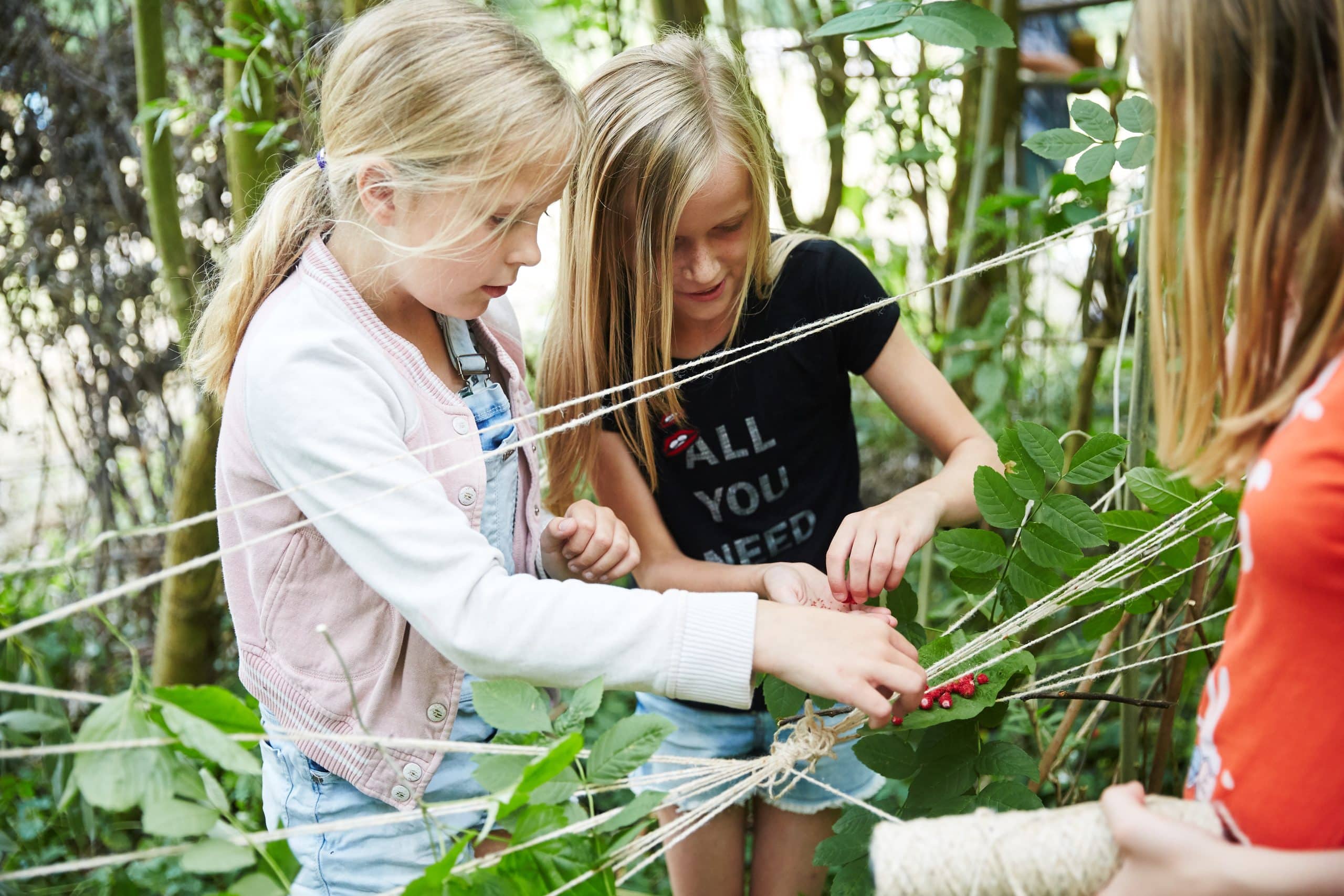 Twee kinderen tussen het groen die touwen weven