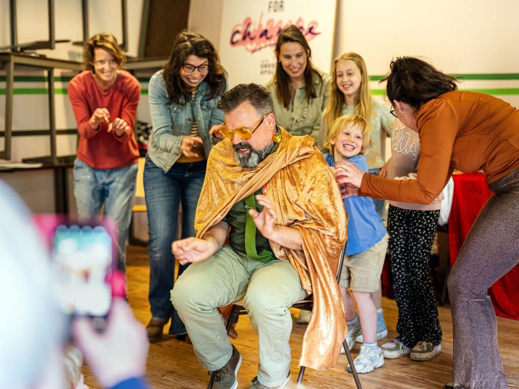 Een acteur met een omslagdoek, met daarachter lachende kinderen en vrouwen