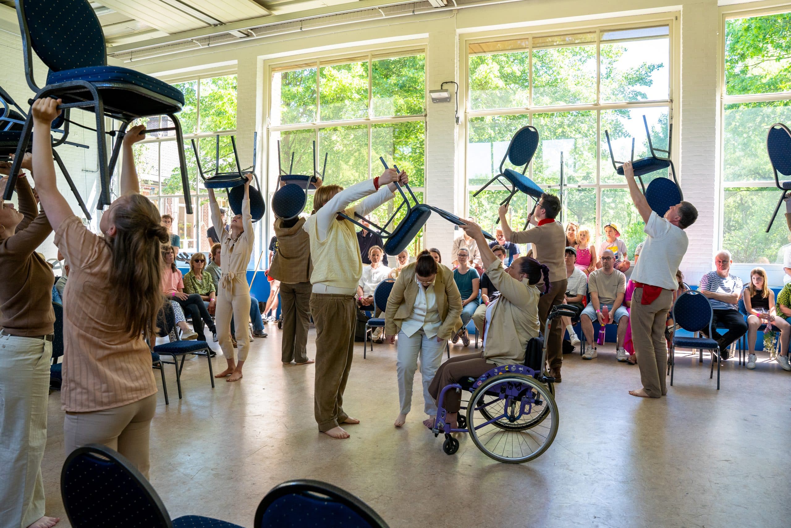 Dansers die met stoelen dansen. 1 van de dansers zit in een rolstoel.