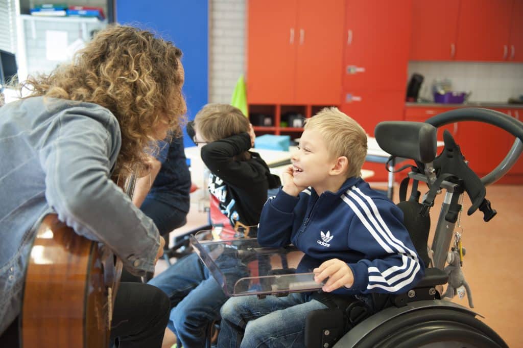 Jongen in rolstoel luistert lachen naar muzikant met gitaar