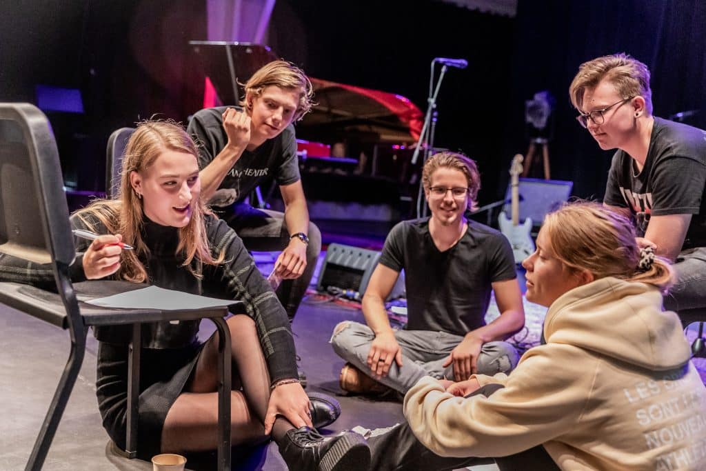 Een groep jonge mensen zit op de grond te overleggen en te schrijven