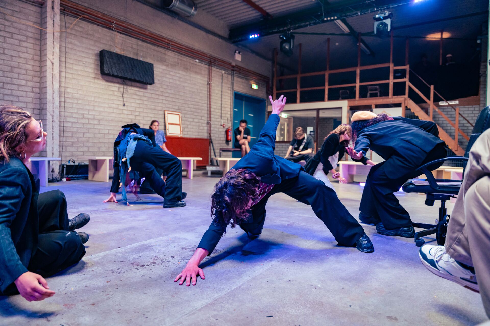Jonge deelnemers voeren een expressieve bewegingsoefening uit in een theateromgeving.