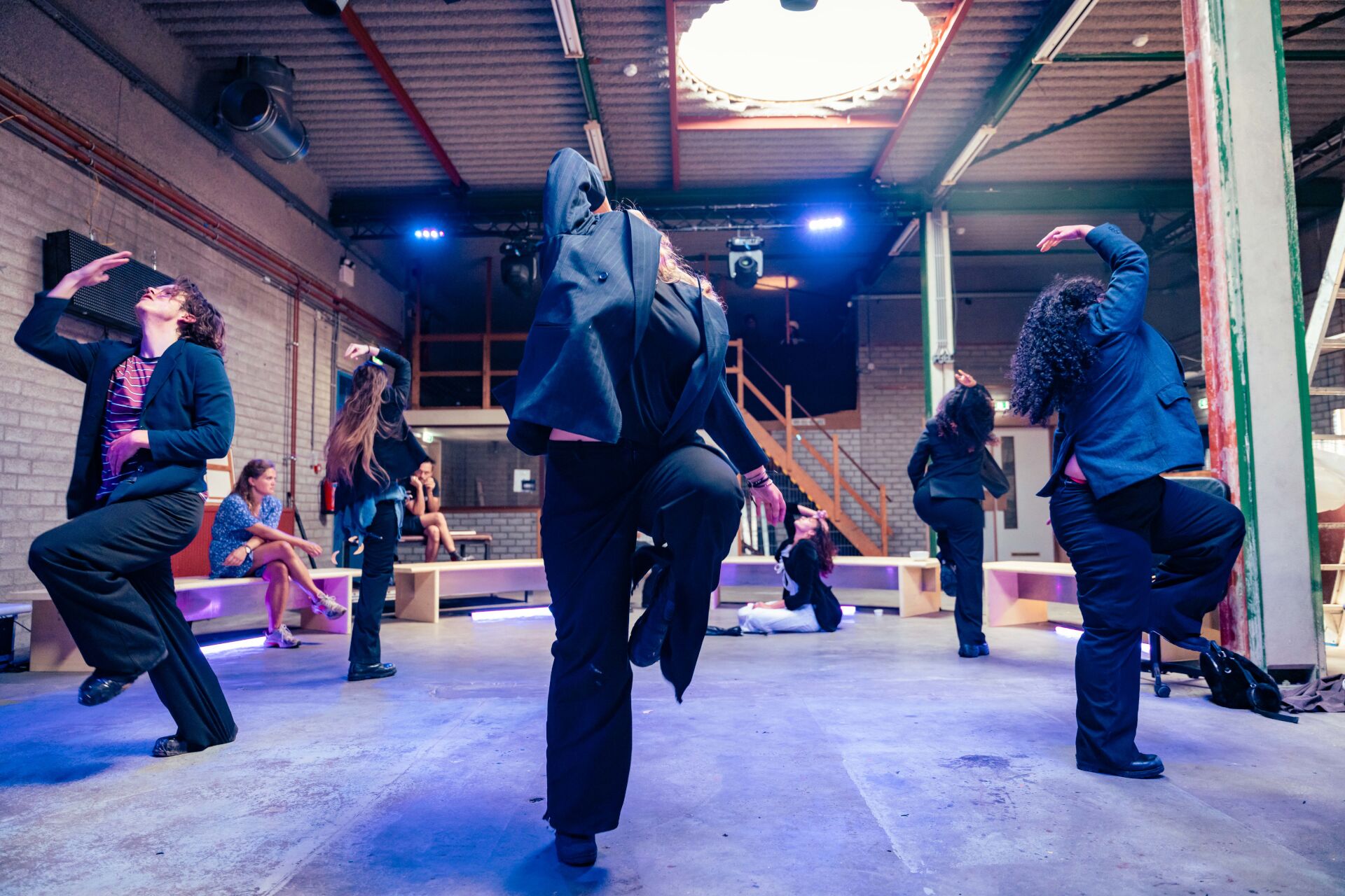 Jonge deelnemers voeren een expressieve bewegingsoefening uit in een theateromgeving.