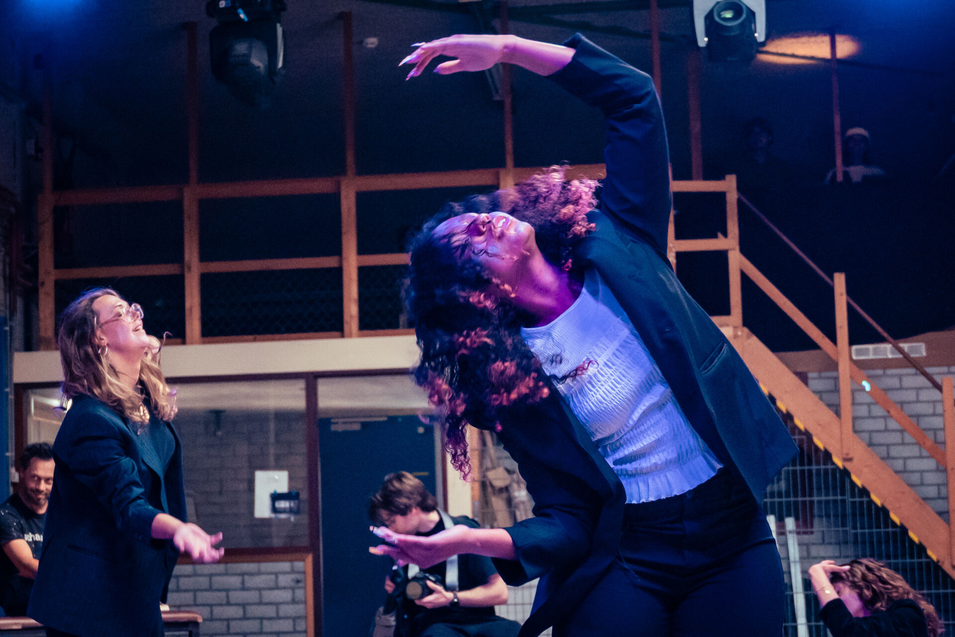 Jonge deelnemers voeren een expressieve bewegingsoefening uit in een theateromgeving.